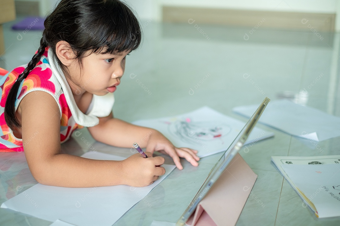 Menina asiática, de 5 a 6 anos, praticando origami usando videoclipes ou estudando on-line via tablet em casa