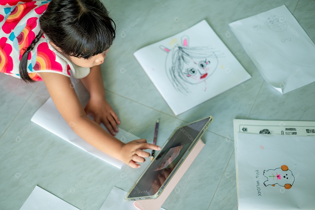 Menina asiática, de 5 a 6 anos, praticando origami usando videoclipes ou estudando on-line via tablet em casa
