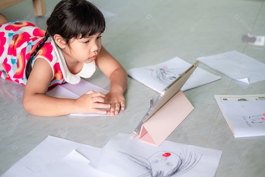 Menina asiática, de 5 a 6 anos, praticando origami usando videoclipes ou estudando on-line via tablet em casa