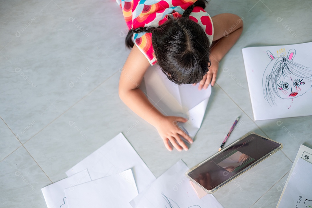 Menina asiática, de 5 a 6 anos, praticando origami usando videoclipes ou estudando on-line via tablet em casa