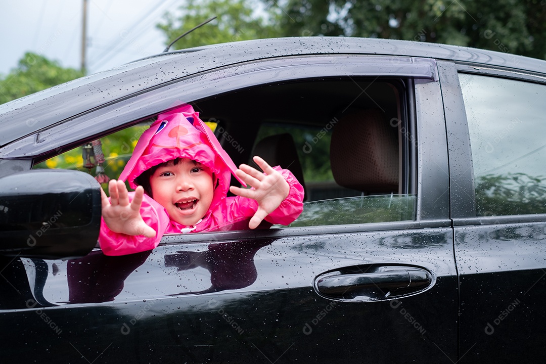 Menina asiática vestindo uma capa de chuva rosa no carro.
