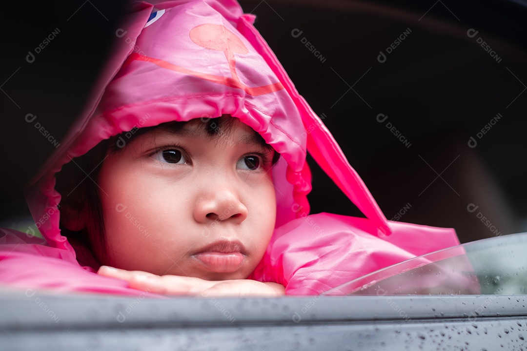 Menina asiática vestindo uma capa de chuva rosa no carro.