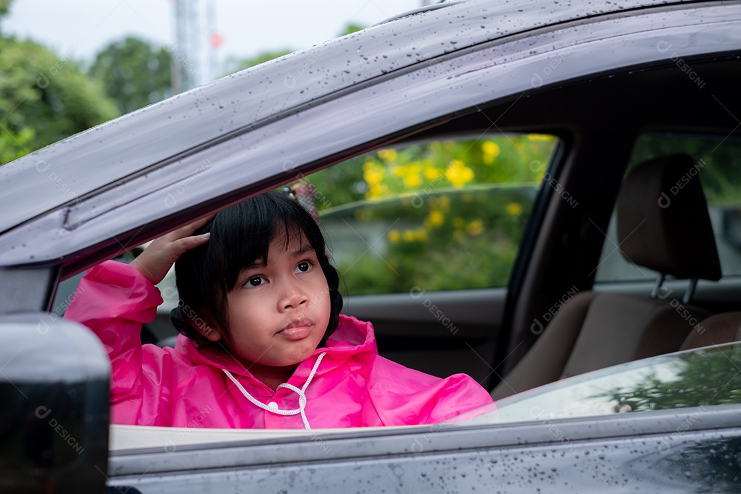 Menina asiática vestindo uma capa de chuva rosa no carro.