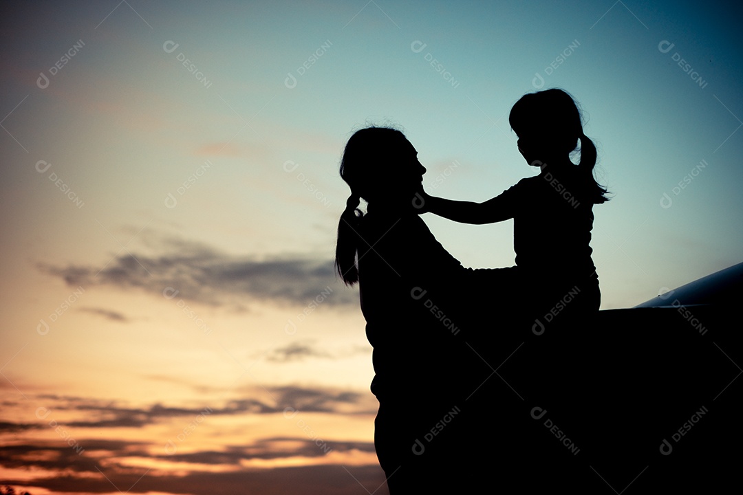 Silhueta de uma garota sentada na parte de trás do carro e aproveitando sua mãe e o pôr do sol laranja