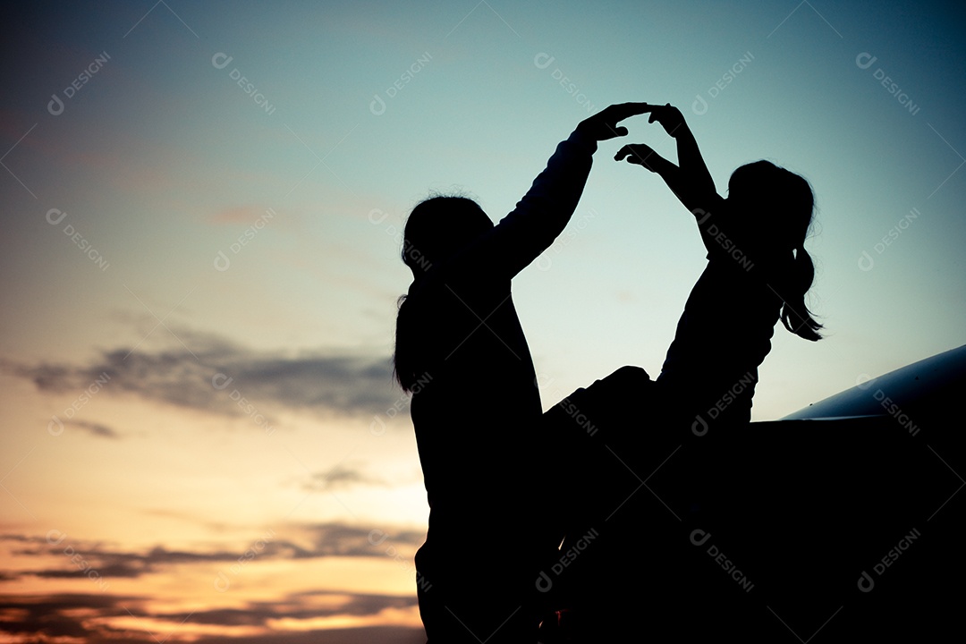 Silhueta de uma garota sentada na parte de trás do carro e aproveitando sua mãe e o pôr do sol laranja