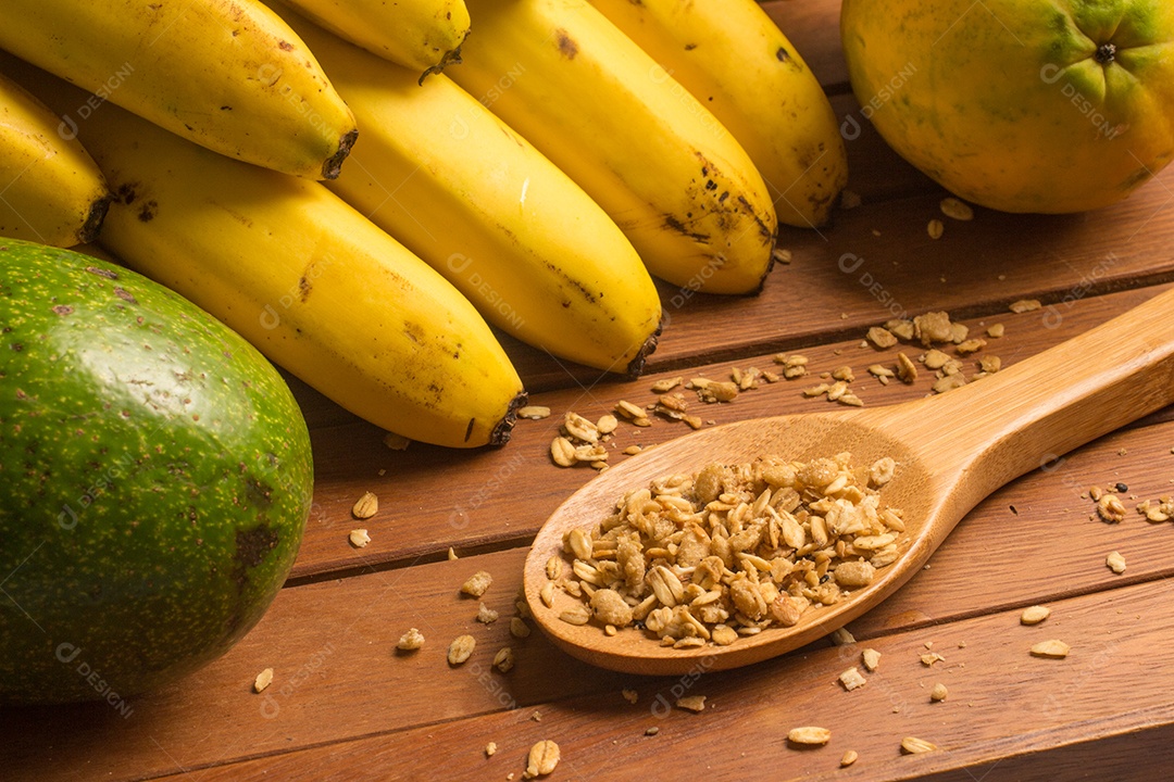 Banana, mamão, abacate e granola sobre uma mesa de madeira