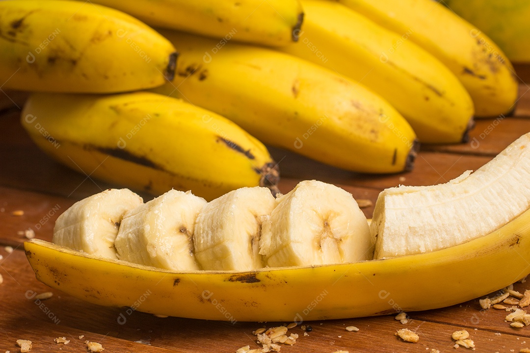 Banana fatiada e granola sobre uma mesa de madeira.