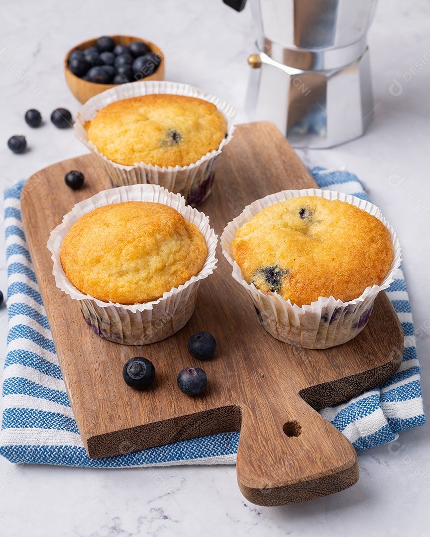 Muffins de mirtilo com frutas sobre tábua de madeira.