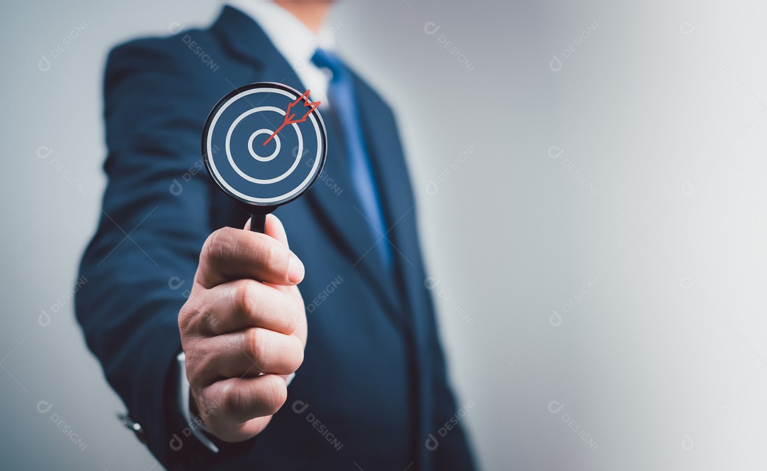 A mão do empresário está segurando uma lupa mostrando um ícone de alvo. Metas de negócios e conceitos objetivos.