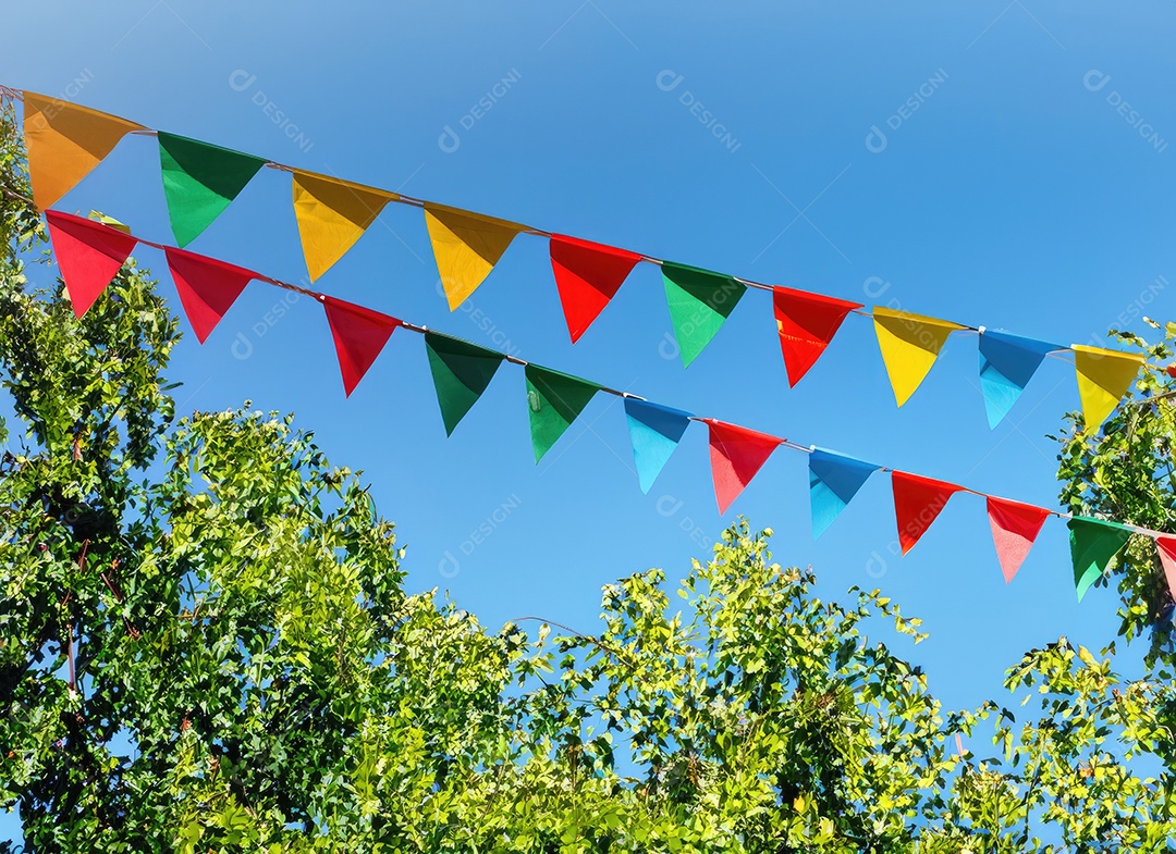 Decoração de corda de flâmula colorida em folhagem de árvore verde no céu azul, fundo de festa de verão.