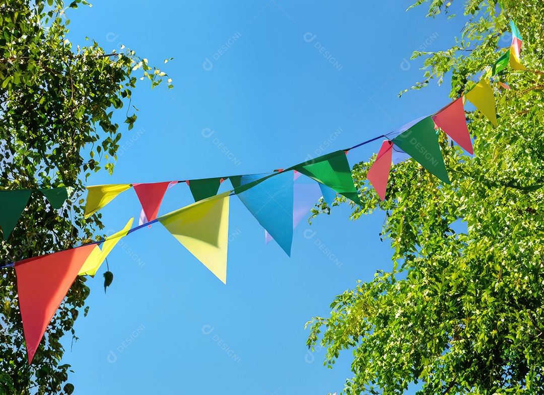 Decoração de corda de flâmula colorida em folhagem de árvore verde no céu azul, fundo de festa de verão.