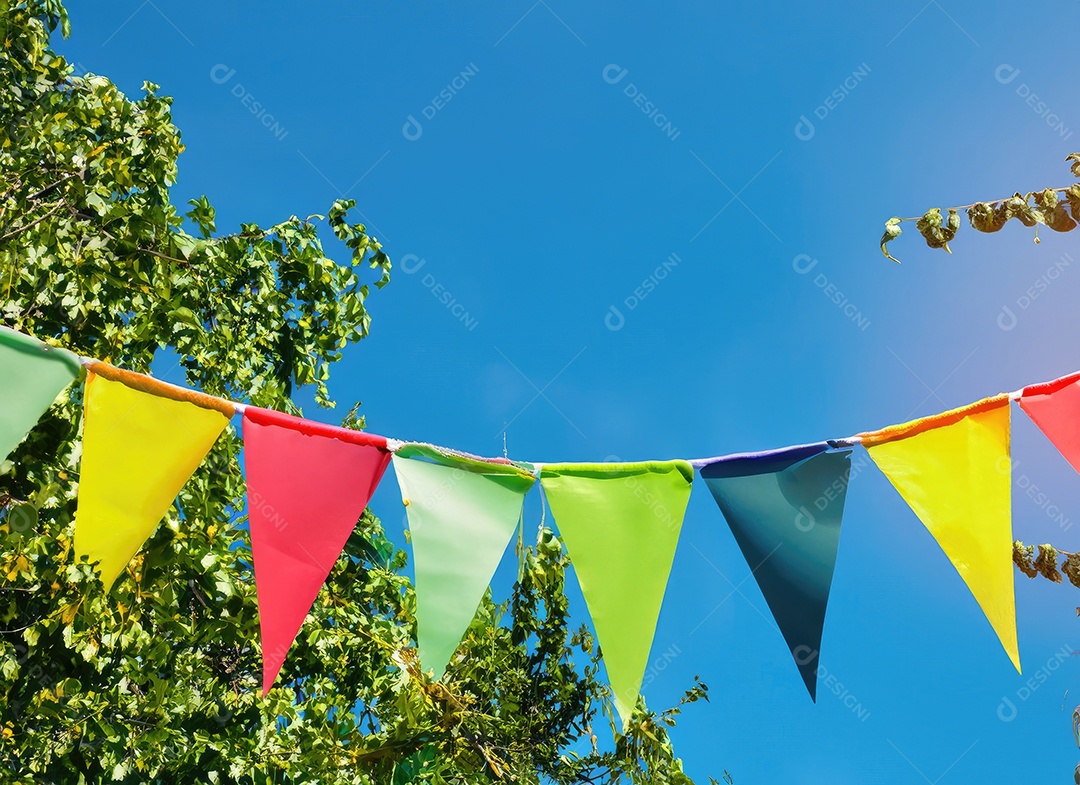 Decoração de corda de flâmula colorida em folhagem de árvore verde no céu azul, fundo de festa de verão.