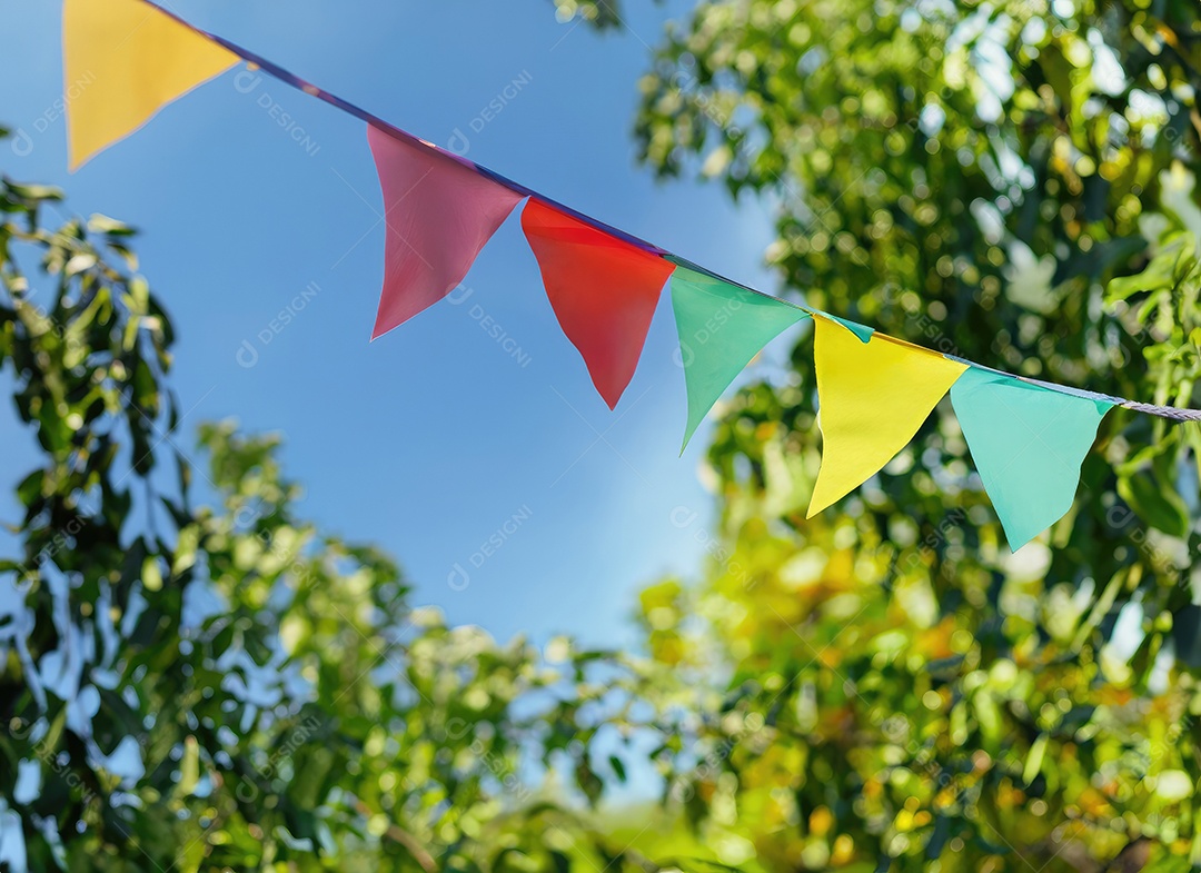 Decoração de corda de flâmula colorida em folhagem de árvore verde no céu azul, fundo de festa de verão.