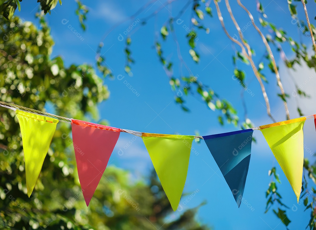 Decoração de corda de flâmula colorida em folhagem de árvore verde no céu azul, fundo de festa de verão.
