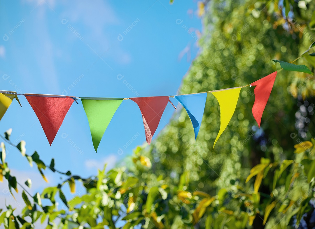 Decoração de corda de flâmula colorida em folhagem de árvore verde no céu azul, fundo de festa de verão.