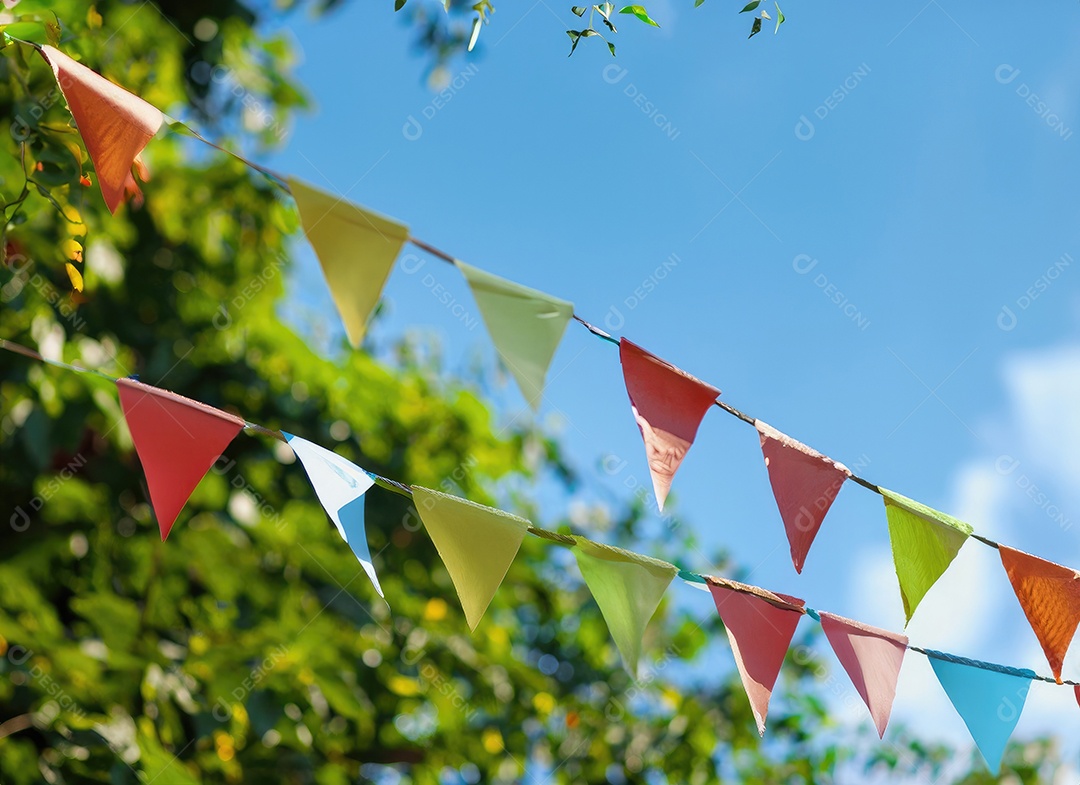 Decoração de corda de flâmula colorida em folhagem de árvore verde no céu azul, fundo de festa de verão.