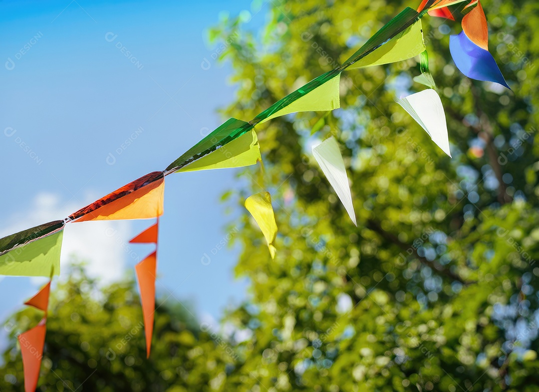 Decoração de corda de flâmula colorida em folhagem de árvore verde no céu azul, fundo de festa de verão.