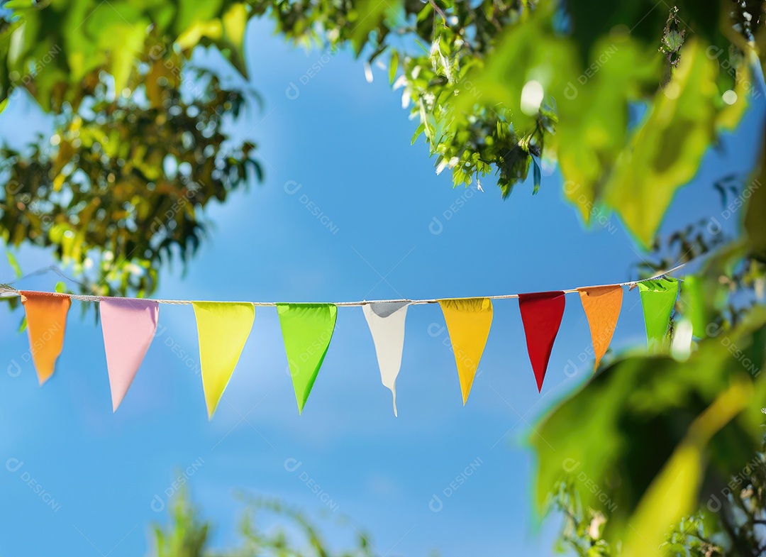 Decoração de corda de flâmula colorida em folhagem de árvore verde no céu azul, fundo de festa de verão.