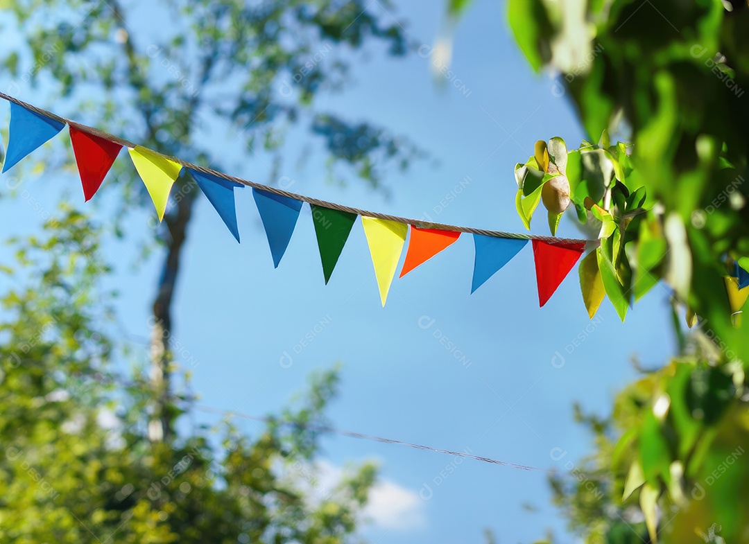 Decoração de corda de flâmula colorida em folhagem de árvore verde no céu azul, fundo de festa de verão.