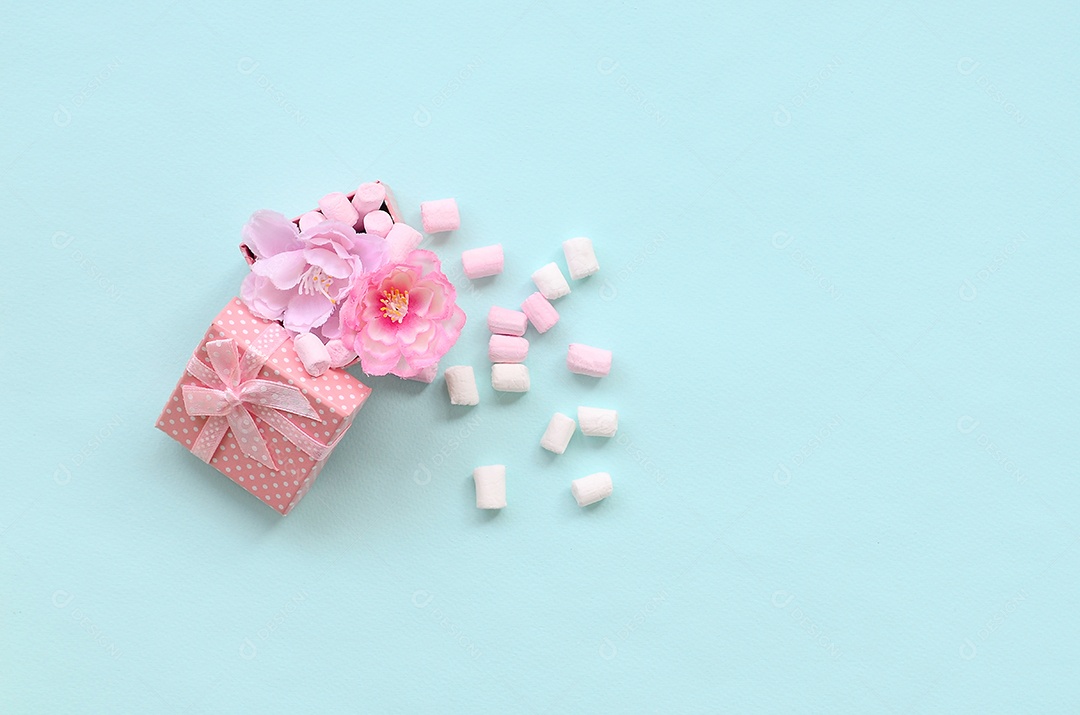 Caixa de presente rosa florida polvilhada com marshmallows sobre fundo azul. Processamento de conceitos metafóricos e cultivo de flores.