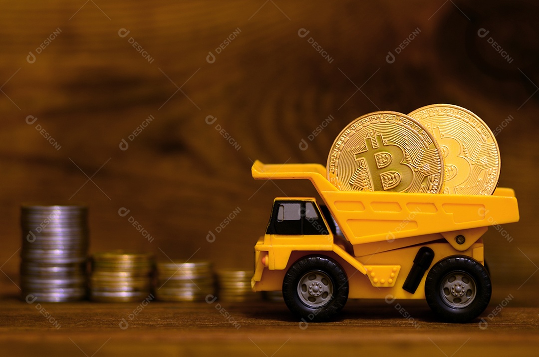 O dumper de brinquedo amarelo carregado com bitcoins dourados brilhantes está ao lado de pilhas de moedas de várias moedas em um fundo de madeira.