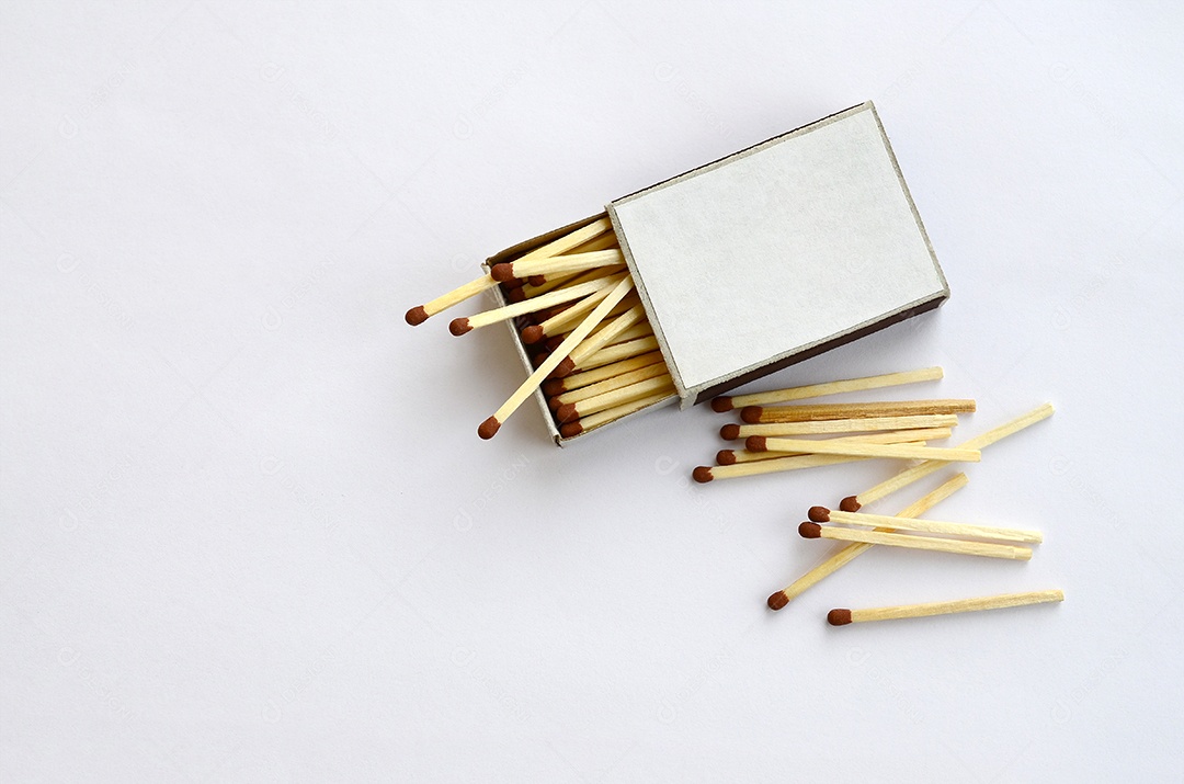 Fósforos de madeira espalhados ao lado de uma caixa de fósforos de papelão