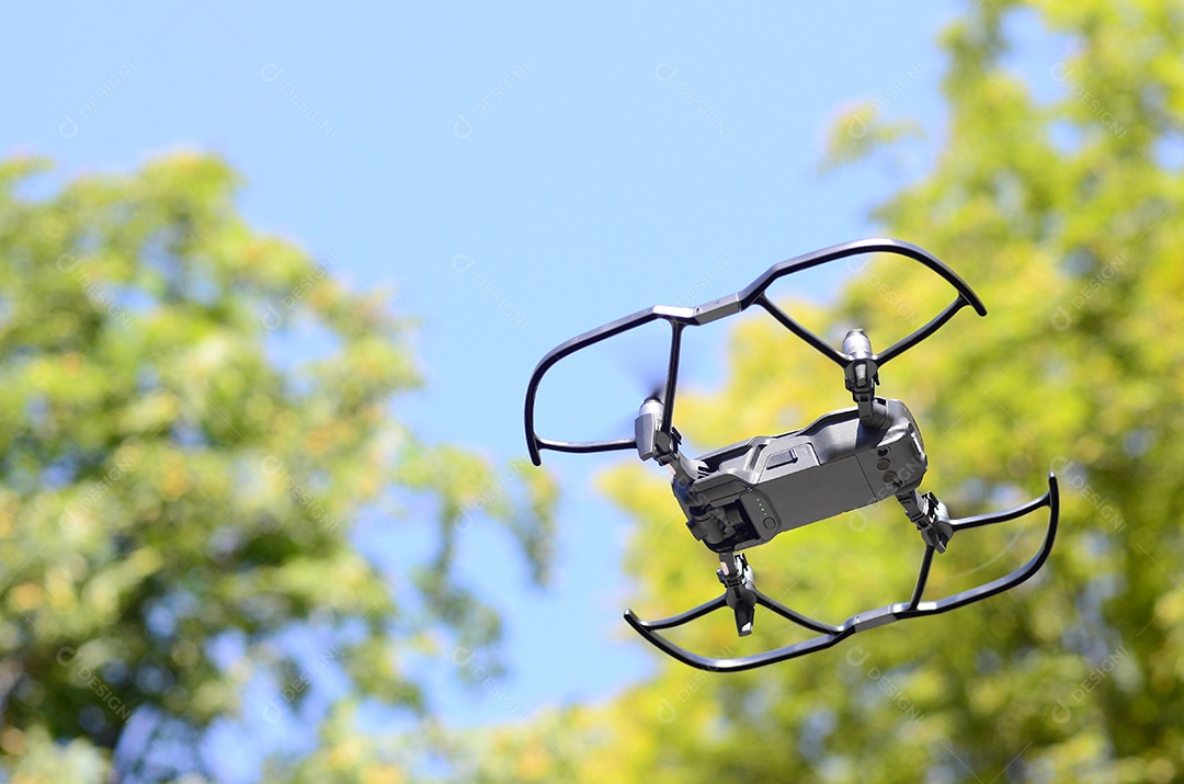 O pequeno helicóptero drone UAV com câmera digital está voando perto das árvores verdes durante o dia