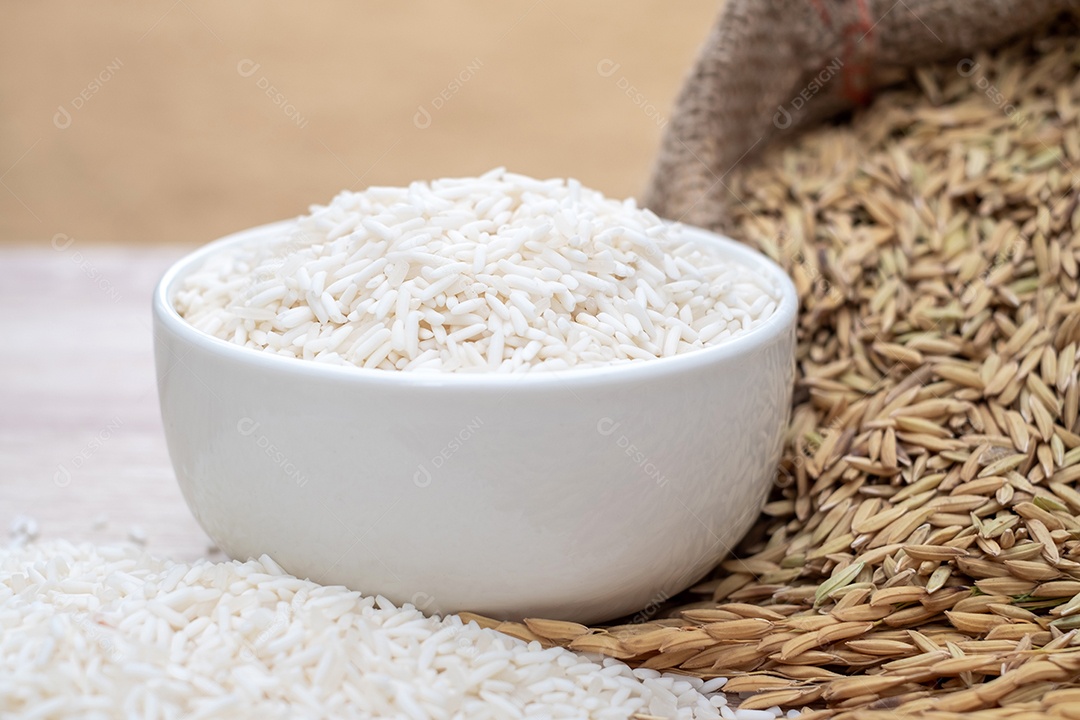 Grãos de arroz branco em tigelas brancas, orelhas e sementes de arroz branco colocadas na mesa de madeira moderna e fundo dourado natural