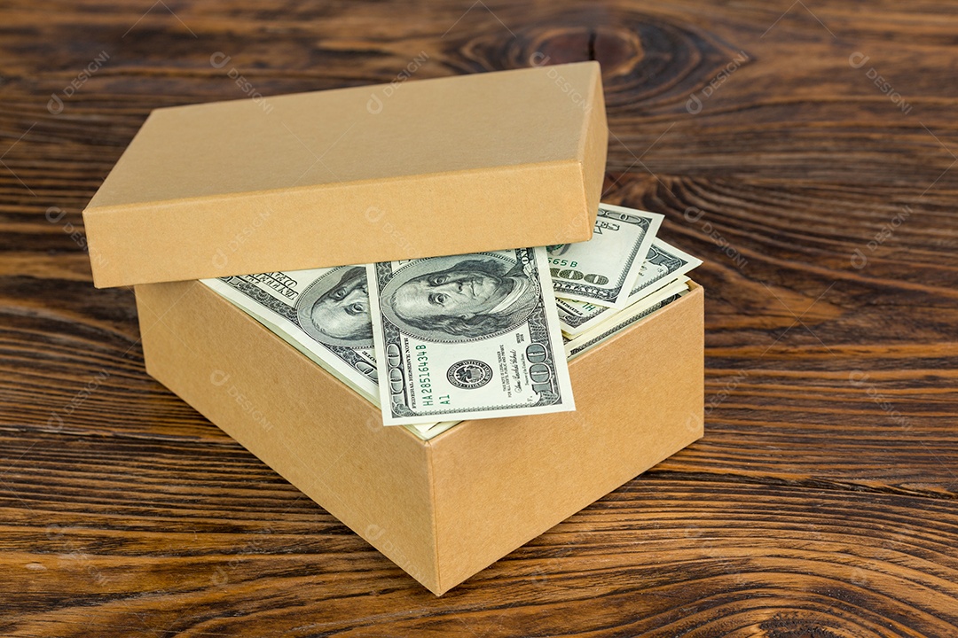 Pequena caixa de papelão cheia de notas de cem dólares em close-up com foco seletivo em fundo de madeira natural