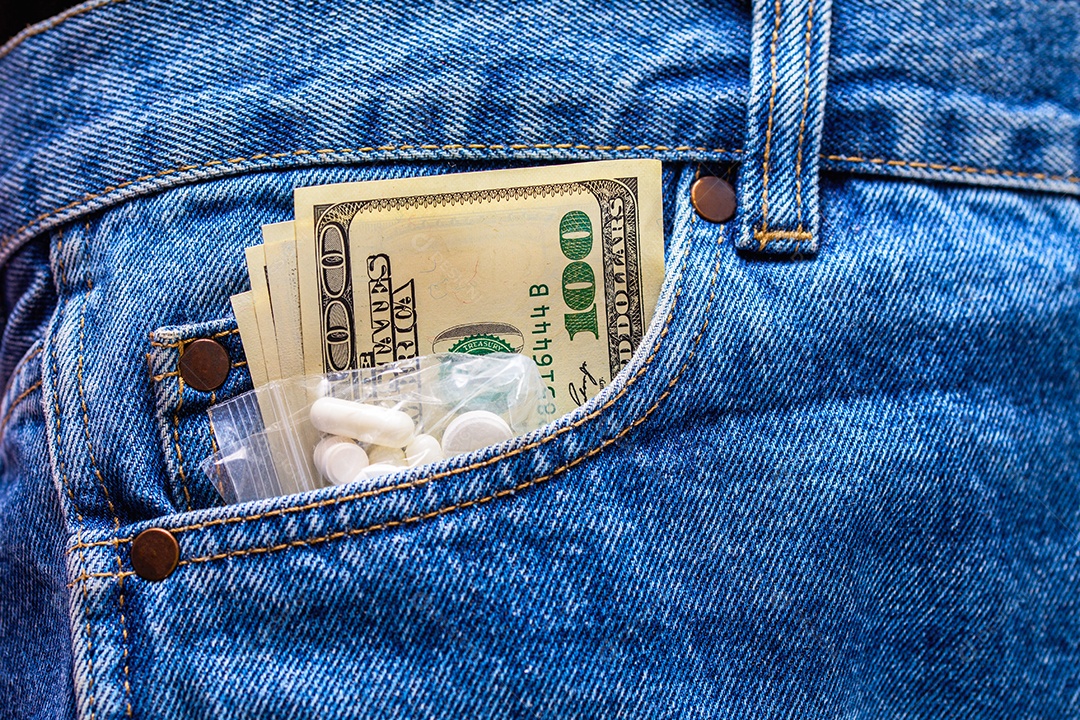 Comprimidos brancos de medicamentos e notas de dólar americano no bolso da calça jeans