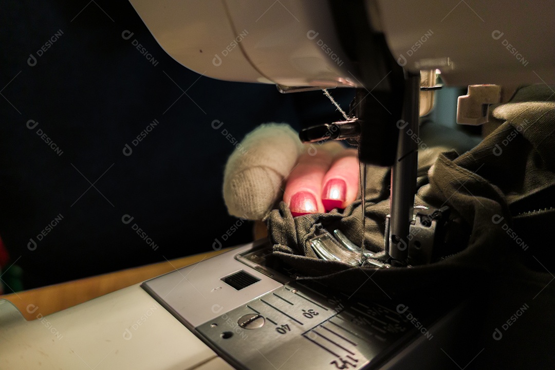 Dedos de uma mulher mais velha inserindo uma linha vermelha na agulha de uma máquina de costura close-up