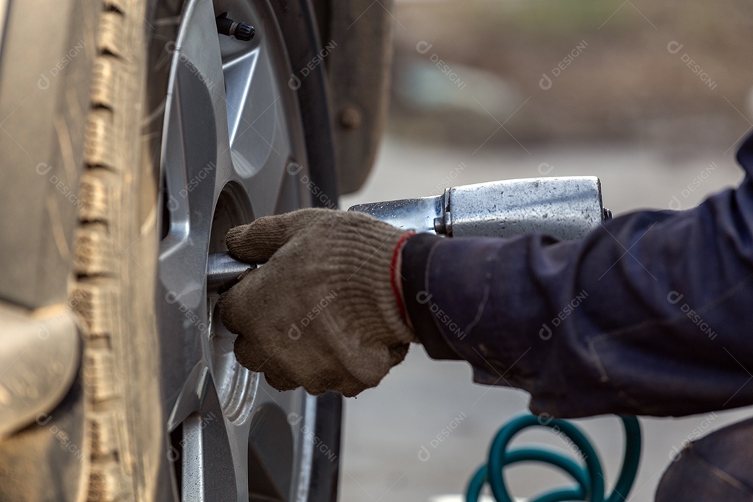 Carro sem roda levantado com macaco hidráulico e chave de impacto pneumática em uma oficina mecânica ao ar livre