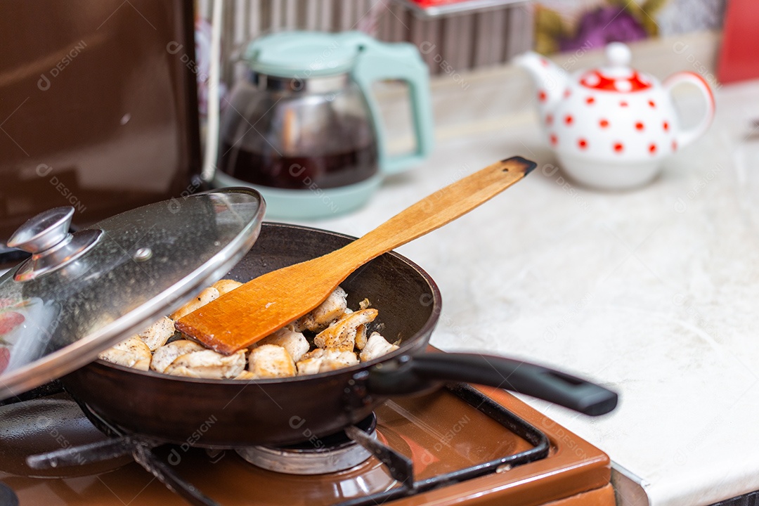 Frango frito em uma panela aberta com pimenta-do-reino moída e espátula de cozinha de madeira