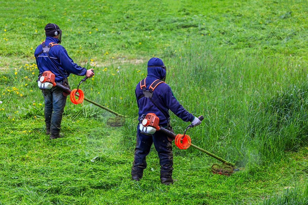 Dois homens cortando grama com aparador de grama e máscara facial aparando grama