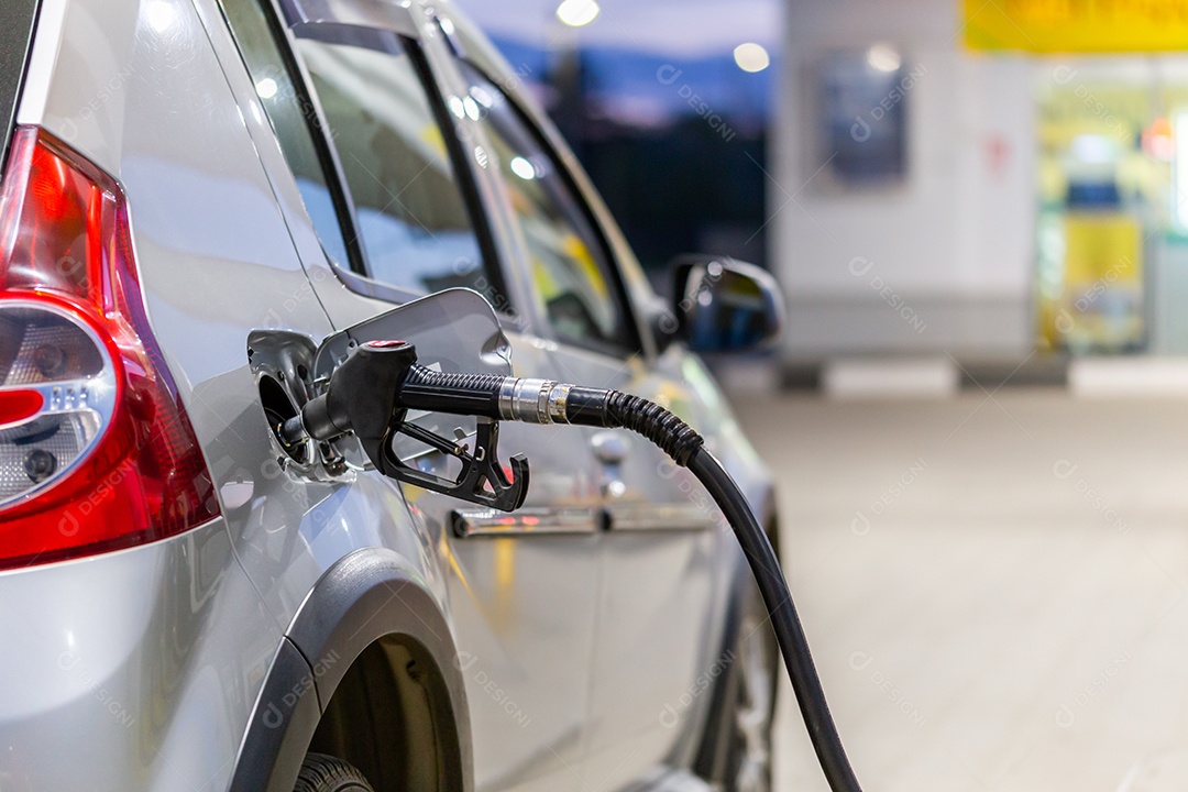 Carro de cor prata metálica reabastecendo em posto de gasolina noturno