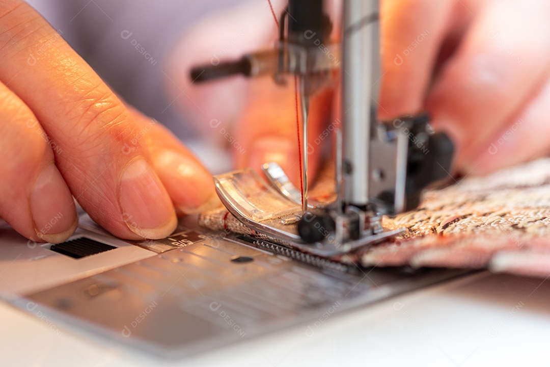 Dedos da avó inserindo uma linha vermelha na agulha de uma máquina de costura close-up
