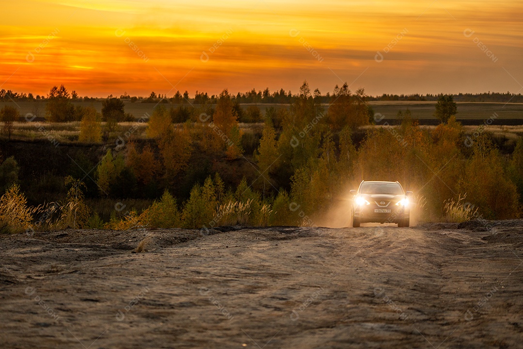 Nissan Qashqai azul subindo em estrada de terra ao pôr do sol dourado de outono