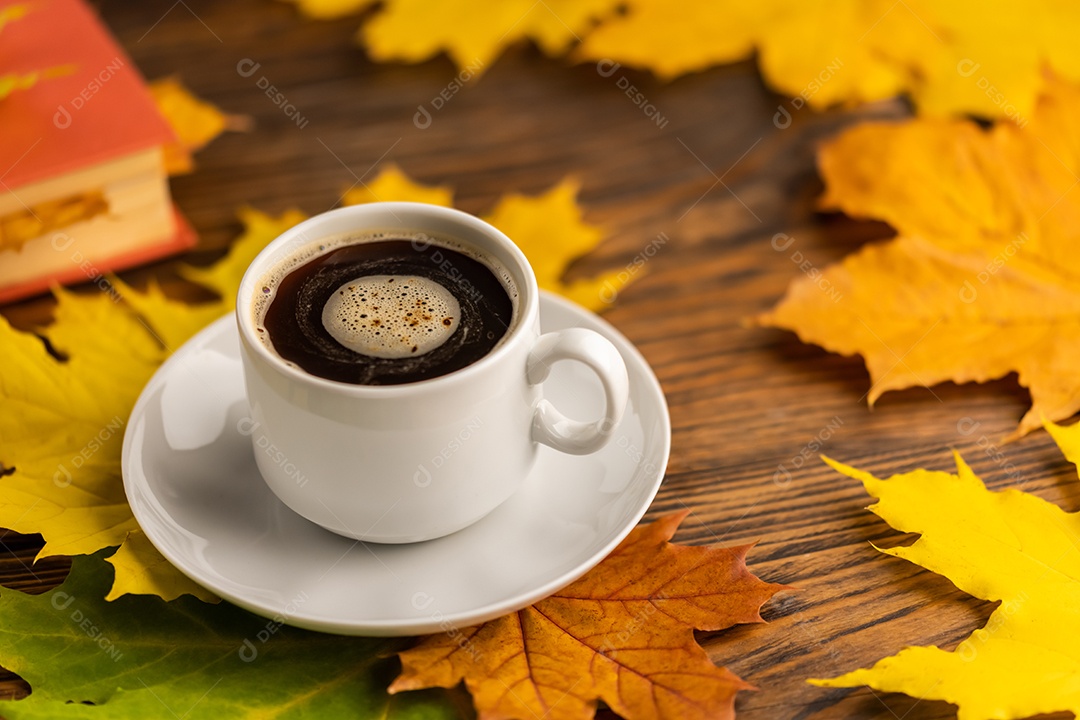 Xícara de café sobre mesa de madeira com livro e folhas coloridas de bordo outonais