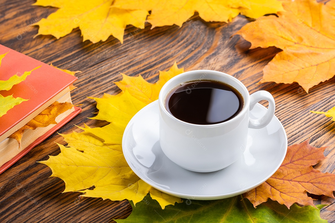 Xícara de café sobre mesa de madeira com livro e folhas coloridas de bordo outonais