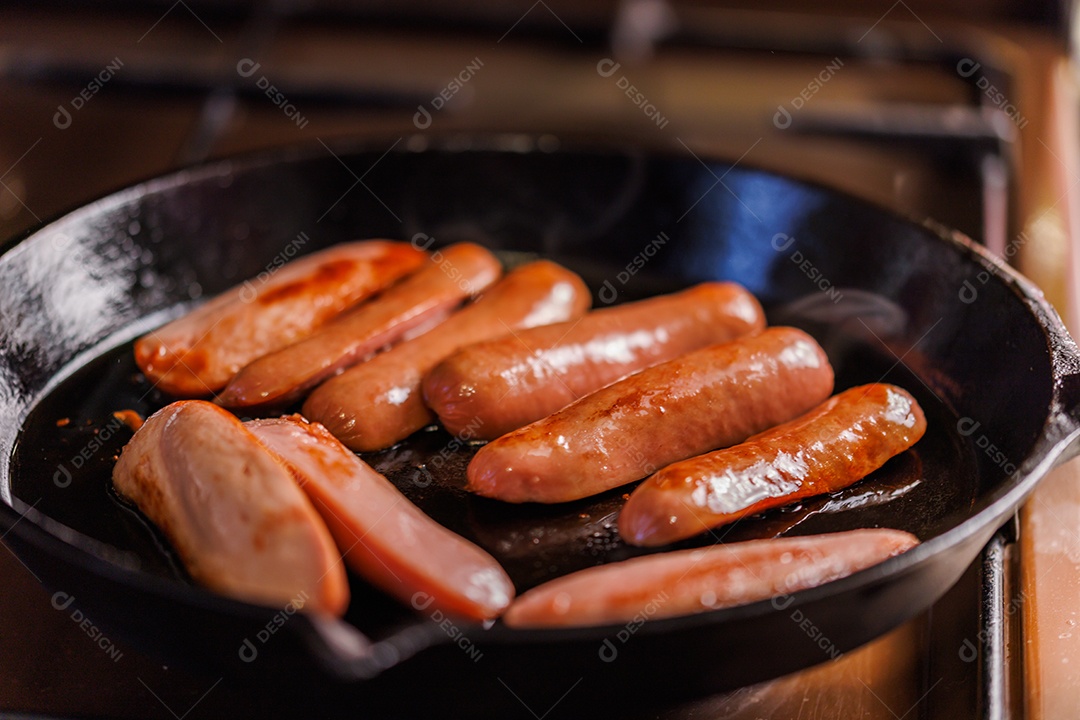 Salsichas cortadas ao meio são fritas em óleo em uma frigideira de ferro fundido preto
