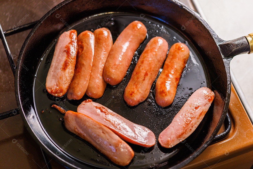 Salsichas cortadas ao meio são fritas em óleo em uma frigideira de ferro fundido preto