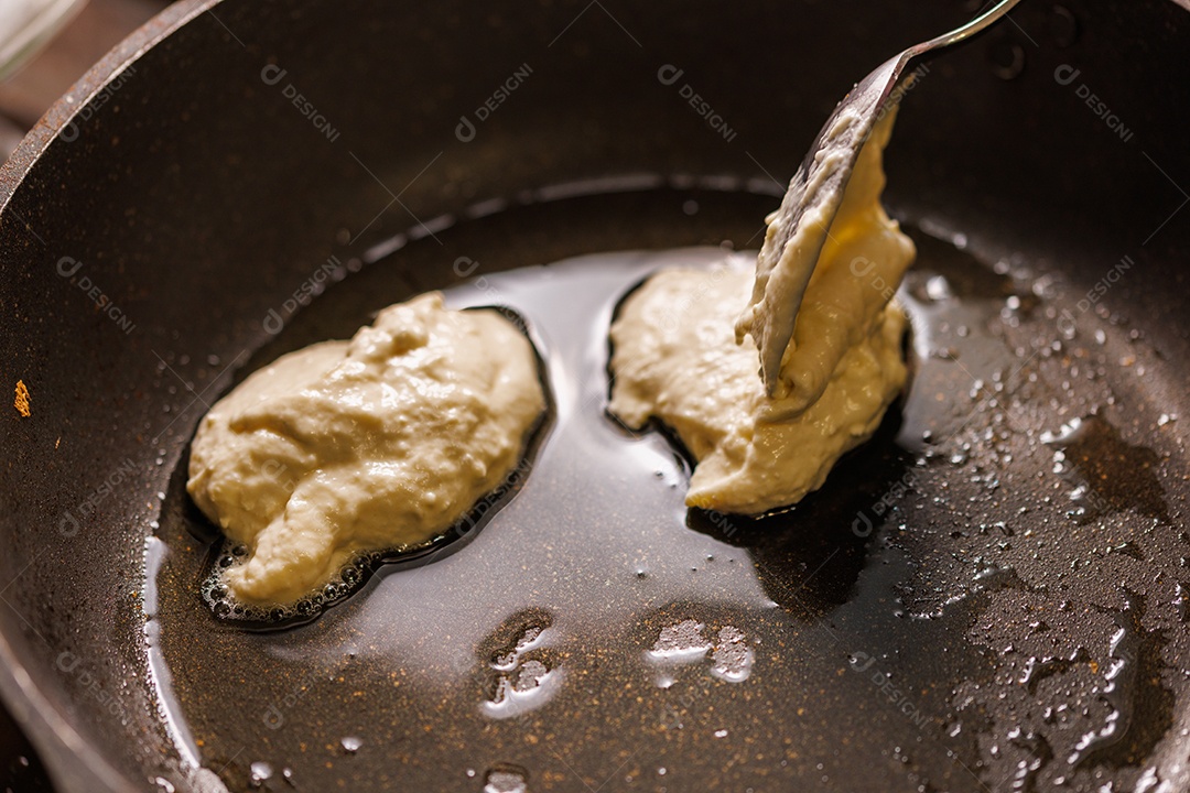 Mãos com garfos virando massa semilíquida fritando em frigideira de ferro fundido