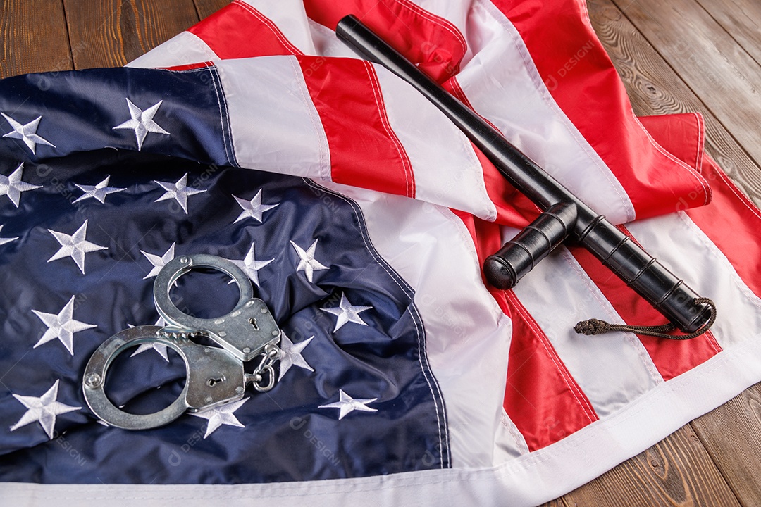 Algemas de metal prateado e cassetete de polícia perto da bandeira dos EUA em superfície de madeira