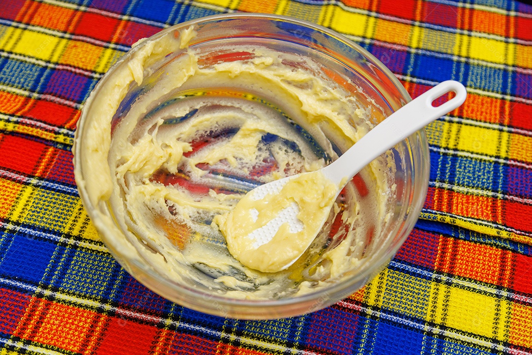 Grande tigela de vidro com sobras de massa e espátula de plástico sobre fundo de toalha colorida