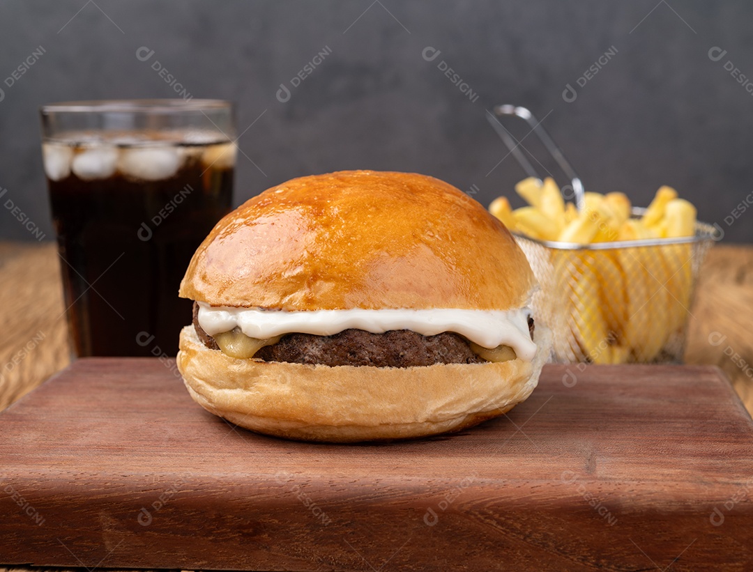 Cheeseburger com maionese sobre tábua de madeira com batata frita e refrigerante.