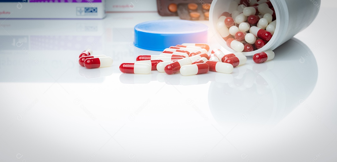 Comprimido de cápsulas vermelhas e brancas derramado de uma garrafa de plástico branca.