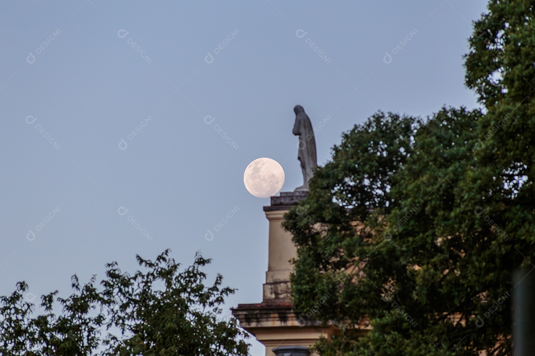 Pôr da lua no céu com estátua de fundo