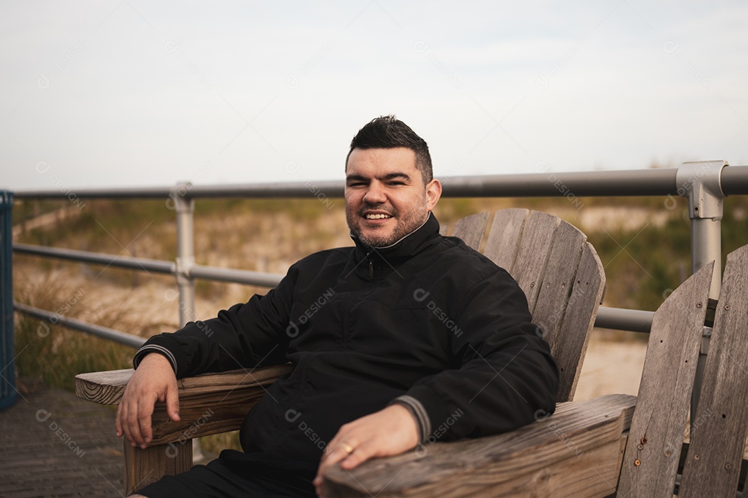 Um adulto sorridente sentado em uma grade de madeira, aproveitando o ar livre.