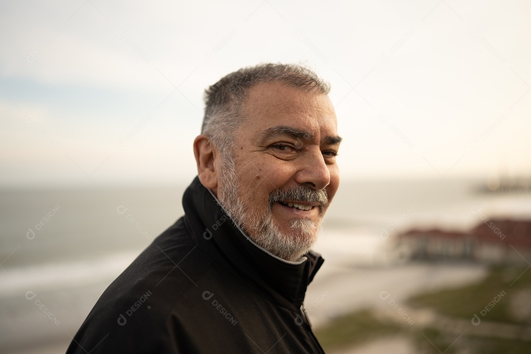 Um homem sênior sorridente na praia, apreciando o mar e o céu.