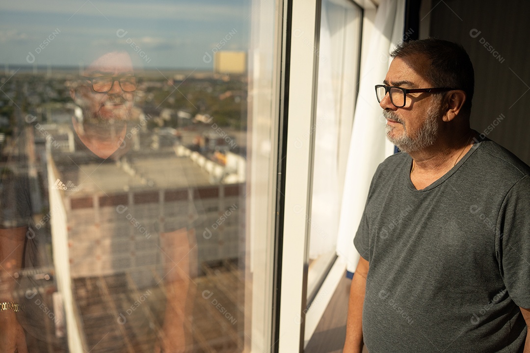 Reflexo da janela de um homem de óculos olhando para um prédio.